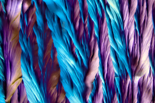 Mikrokristall-Fotografie von Paracetamol – leuchtende Kristallstruktur in Blau, hellem Violett mit feinen, diagonalen Ausläufern.